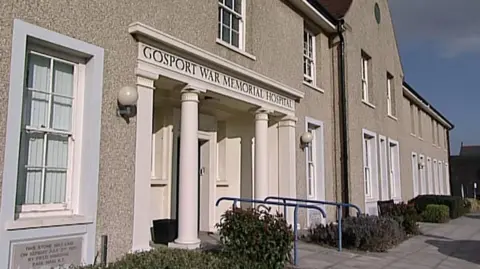 BBC The front entrance of the hospital, a light-coloured building of at least two storeys, is flanked by two white columns. The words "Gosport War Memorial Hospital" are on the side of the building above the doorway.