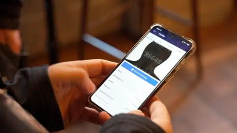 BBC A close up of a mobile phone displaying an app. A blacked out profile picture can be seen along with boxes where names, ages and details can be filled out