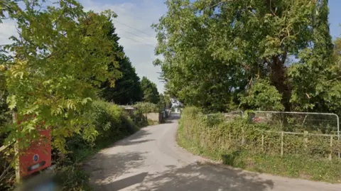 A tarmac road with trees and greenery either side showing the entrance to the Springway Lane site.