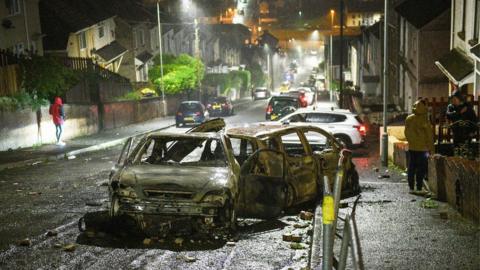 Burned out cars in a street in Mayhill following disorder