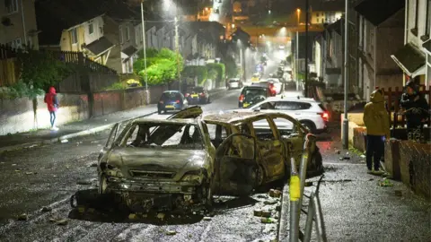 Robert Melen Burned out cars in a street in Mayhill following disorder