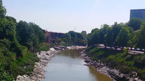 The Avon New Cut near Temple Meads station on a sunny day, with the yellow "banana bridge" crossing the river and trees lining the river.