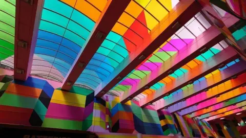 Aaron Law Una pasarela cubierta ha sido pintada con todos los colores del arcoíris en diferentes patrones para crear una obra de arte muy dramática e imponente.
