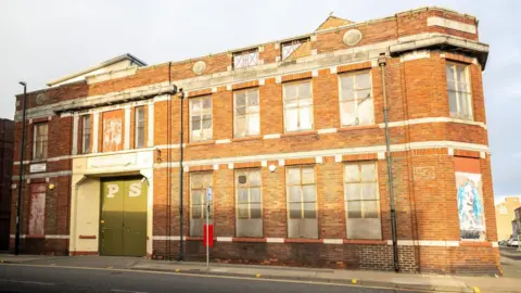 Sunderland City Council The two-storey red-bricked building has large green doors with the letters "P" and "S" painted on them. There are several large boarded-up windows.