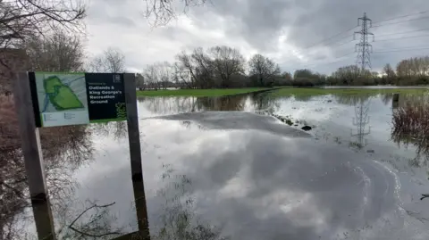 A view of flooded Oatlands & King George's Recreation Ground in Oxford. The sign with the name of the park is in vision. The rounds are saturated.