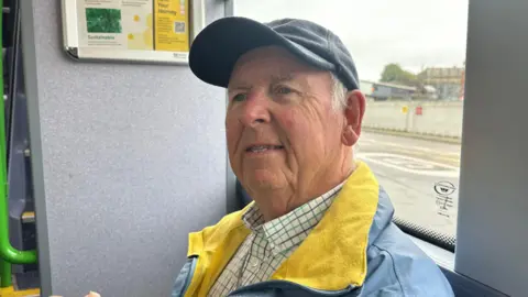 BBC Leslie Downes sat on a Bee Network bus wearing a cap 