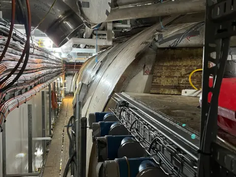 A large cylindrical tank on a ship with lots of wiring in the left hand of the picture