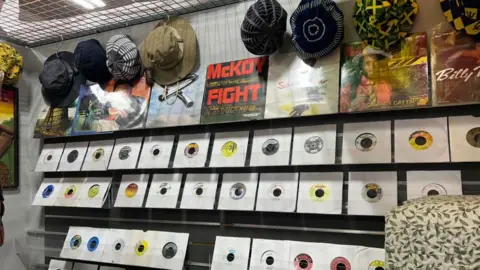 Records stand on shelves with different coloured hats hanging above.