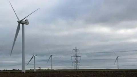Four large wind turbines in fields along with a pylon and cables