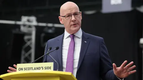 John Swinney, who is bald with glasses, at a podium