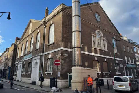 Brick Lane Mosque - a large brick building on the corner of two roads with pedestrians walking in front of it