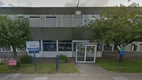 Google The exterior of the pre-fabricated two-storey mental health unit in the grounds of Lister Hospital in Stevenage. A sign reads 'Mental Health Unit, Lister Hospital'. There is an entrance with two sets of glass automatic doors.