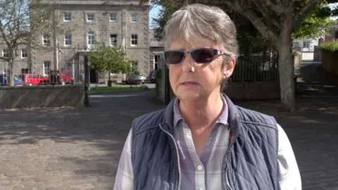 A woman with a purple and white striped shirt on and a gilet.