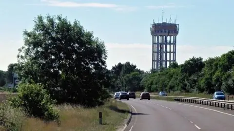 David Dixon/Geograph A view of the Trimley St Mary water tower - a large concrete and steel tower with telecommunication equipment on the top of it - pictured from the A14, on which cars are travelling.