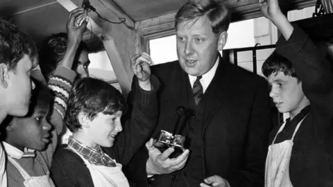 Getty Images Roy Hattersley campaigning to be an MP in 1963. He is in a school surrounded by a class of boys.