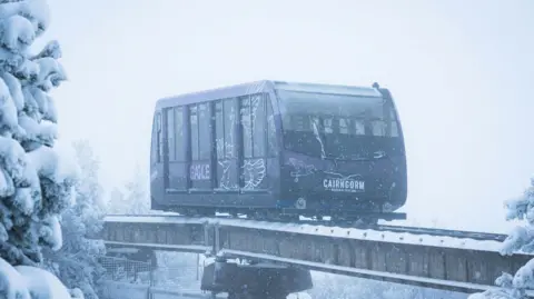 A carriage on the rails of the Cairngorm Funicular. It is snowing and snow gives a hazy blue effect to the scene.