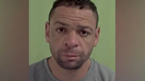 Doherty's police mugshot. He has short dark hair and stubble and is wearing a grey sweatshirt.