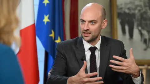 Jeff Overs / BBC French Foreign Minister Jean-Noël Barrot speaking to the BBC's Laura Kuenssberg. He is wearing a dark gray suit, white shirt and tie with black stripes