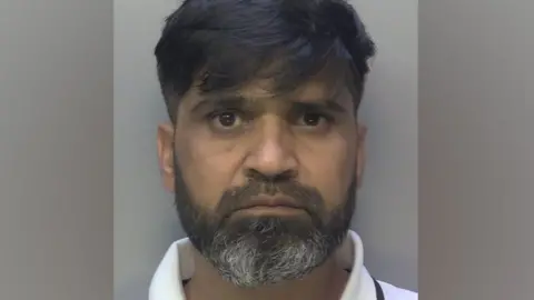 Surrey Police Police mugshot of Urfan Sharif. He has a beard and is looking straight at the camera.