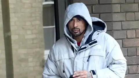 A man wearing a grey hoodie and a grey jacket. He is holding a coffee cup.