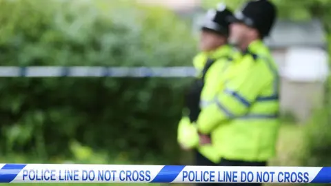 PA Media Blurred imaged of two police officers in uniform stood at a police cordon.