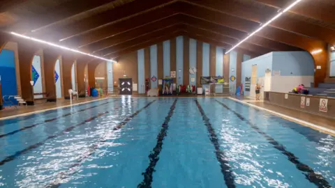 Telford and Wrekin Council A swimming pool with blue tiles. The roof is wooden, and there are wood panels on the walls