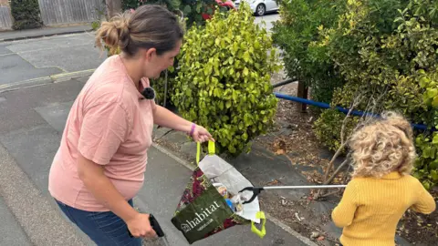 Jaimielee Rendall/BBC A woman and her young daughter are litter picking next to some bushes 