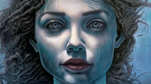 La Vida Liverpool The mural is a close up of a young woman's face painted in shades of blue, giving the impression she is under water. She has long dark hair that appears to be floating in the water behind her.