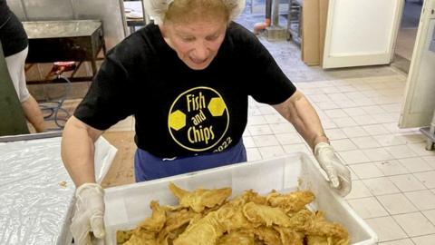 A woman holding a large box of battered fish