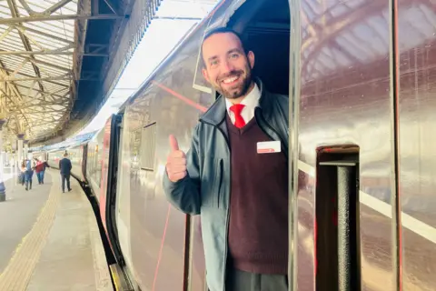 Train driver - Martin Wallace - smiling at camera at cab door, with thumb up.
