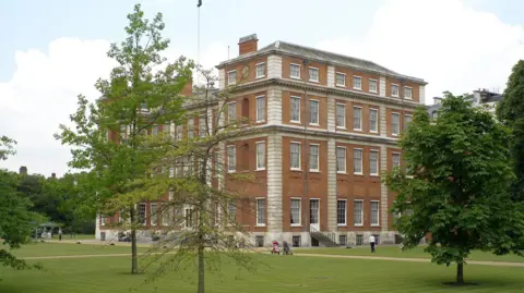 Gavin Gardiner The facade of the red-brick Grade I listed mansion, surrounded by neatly mowed lawn and green, leafy trees.