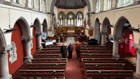 The interior of a Victorian church with pews on either side and pillars 