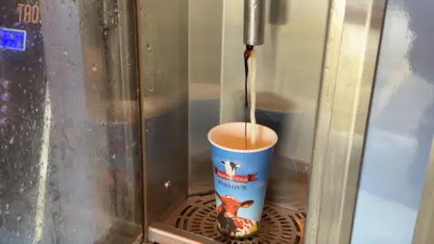 A view of the milk and chocolate flavouring coming out of the milk vending machine into a paper cup.