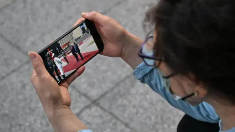 A woman watches a video of US President Donald Trump with China's President Xi Jinping on a mobile phone in Beijing, in May this year