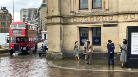 A red London double decker bus with extras dressed in 1940s period clothing 