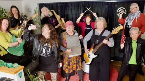 The band performing. Lisa is holding her microphone aloft as she belts out a song. 