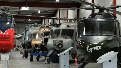 A row of helicopters in a large hangar with information boards in front of each exhibit