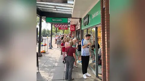 Handout A long line of people queueing outside Specsavers in Formby to purchase eclipse glasses.