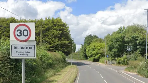 Google A Google street view image of the Bilbrook 30mph road sign, saying Please drive carefully, on Pendeford Mill Lane. Trees can be seen to the right and left of the road. 