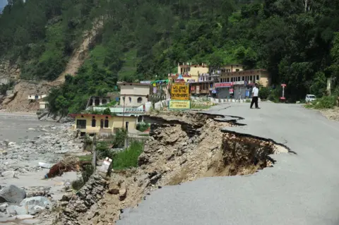 Getty Images A road beside a river has been washed away by flood water in India. A small town can be seen in the background.