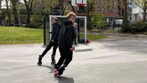 Leo and Noah skating on a hard standing outdoor space.