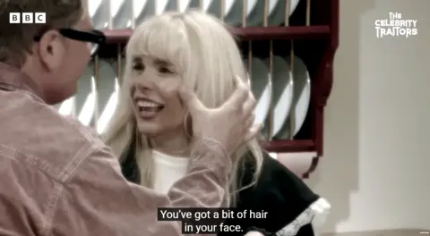 Alan Carr touches Paloma Faith's cheek with his thumb in a scene from The Celebrity Traitors