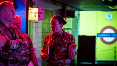 British Army An officer speaks to other soldiers in a disused Tube platform - they are all wearing combat gear.