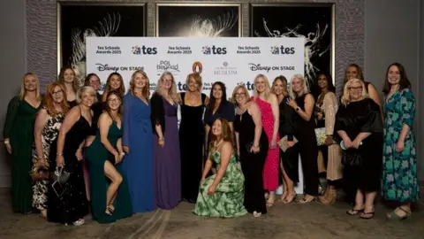A large number of women in ballgowns smiling during an official photograph taken at an award ceremony.
