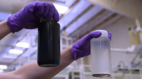 374Water Two bottles are held up - one containing a brown liquid and one containing a clean liquid