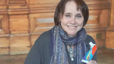 Councillor Zoe Cookson, pictured with short brown hair holds up a used toothpaste tube.