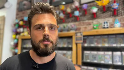 Man with dark hair, a beard and black T-shirt pictured in front of some trading cards