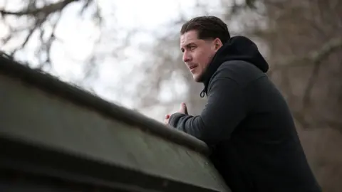 Getty Images A man looks into the distance. He is wearing a black coat. The framing and content of the picture look sombre. 