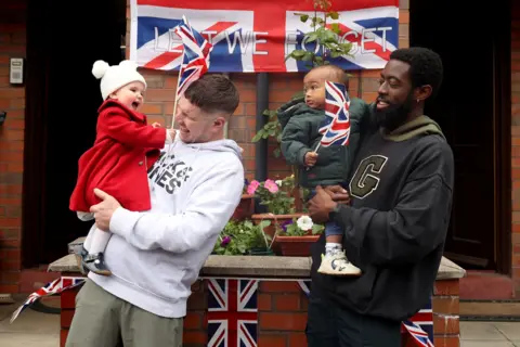 Reuters Two fathers hold their baby children who wave union flags in front of a union flag banner reading 'lest we forget' as they celebrate at a street party in Manchester.