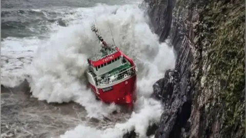 The image shows a red fishing vessel named 'Fastnet' appearing to hit a cliff edge during stormy weather. 